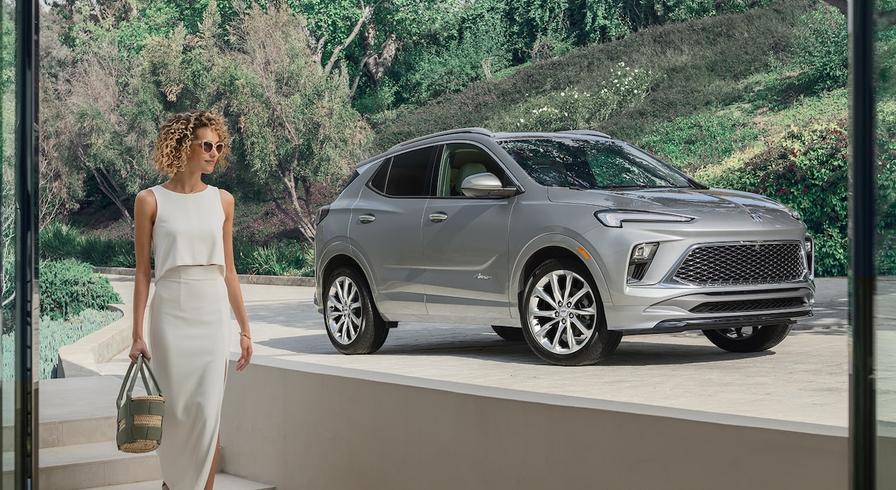 A woman walking into her house with her Buick vehicle parked in the driveway