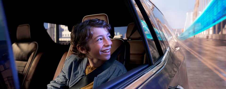 A young boy smiling while looking out the window of a moving vehicle with OnStar.
