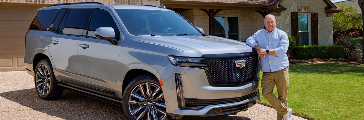 Eric in a blue polo shirt leaning onto the hood of his Cadillac SUV