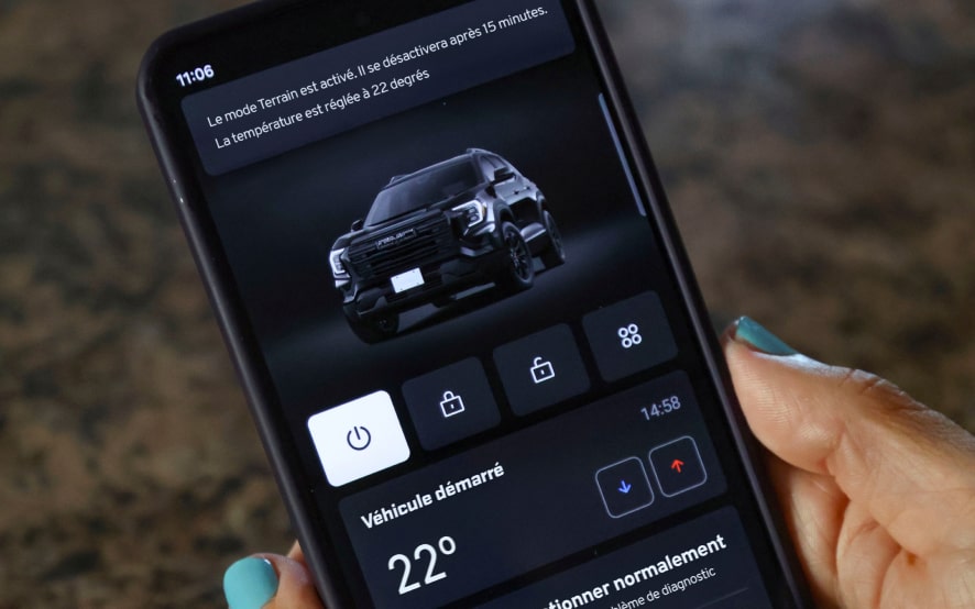 Un téléphone intelligent affiche l’application mobile MyGMC, affichant un GMC Terrain noir ainsi que des services pour véhicules connectés, tels que le démarrage à distance et la commande de la température.