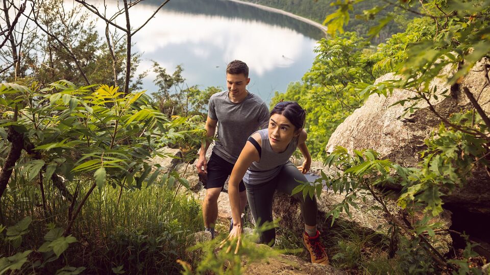 Two people happily hiking up a trail with a lake behind them.