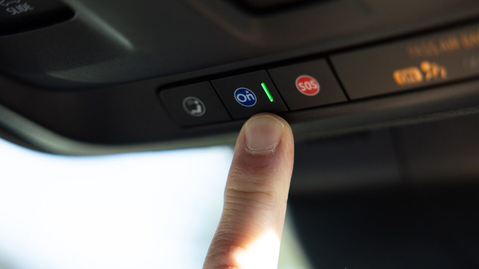 A person's finger pressing the OnStar button inside a Cadillac SUV.