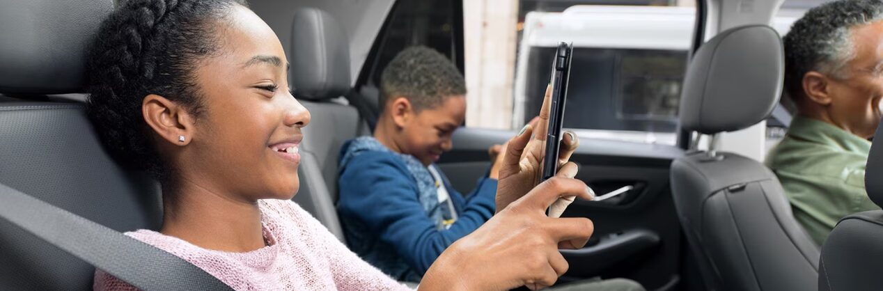 Un garçon et une fille sur la banquette arrière d'une voiture souriant et regardant des tablettes