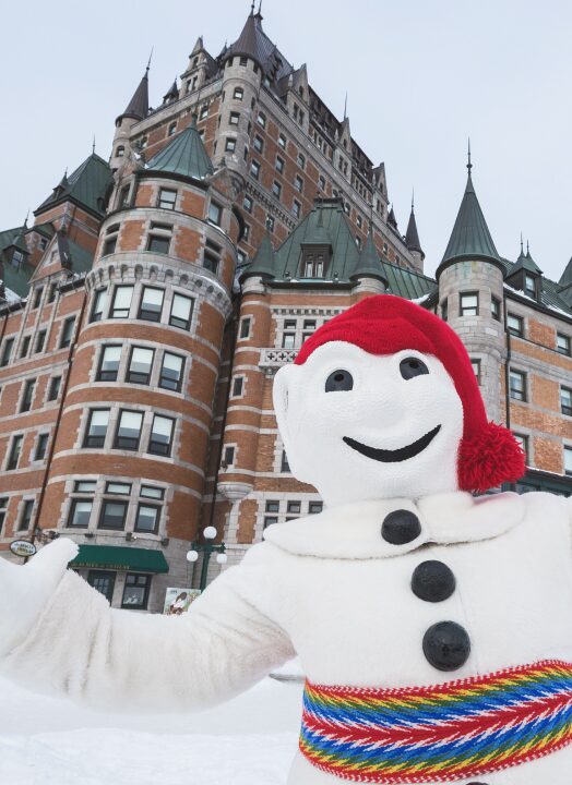 A snowman mascot posing for a camera shot in front of a castle.