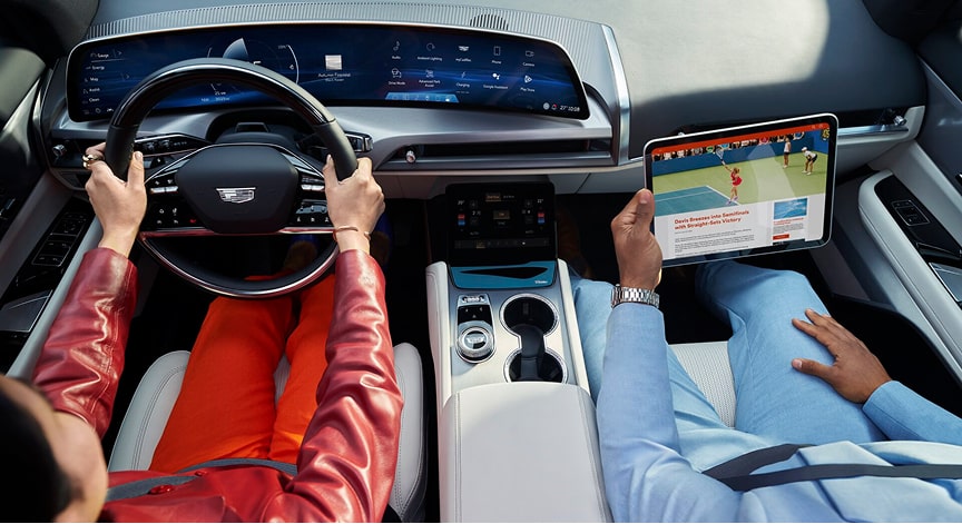 An overhead view inside a Cadillac vehicle with one person driving and another using a tablet.