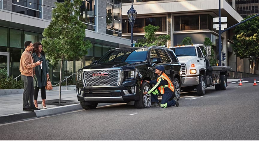 Roadside assistance helping two people with a flat tire on a black GMC SUV.