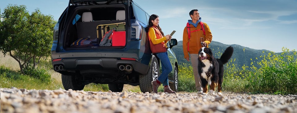 Un VUS GM était stationné sur un sentier pittoresque à côté de deux voyageurs et d’un chien.