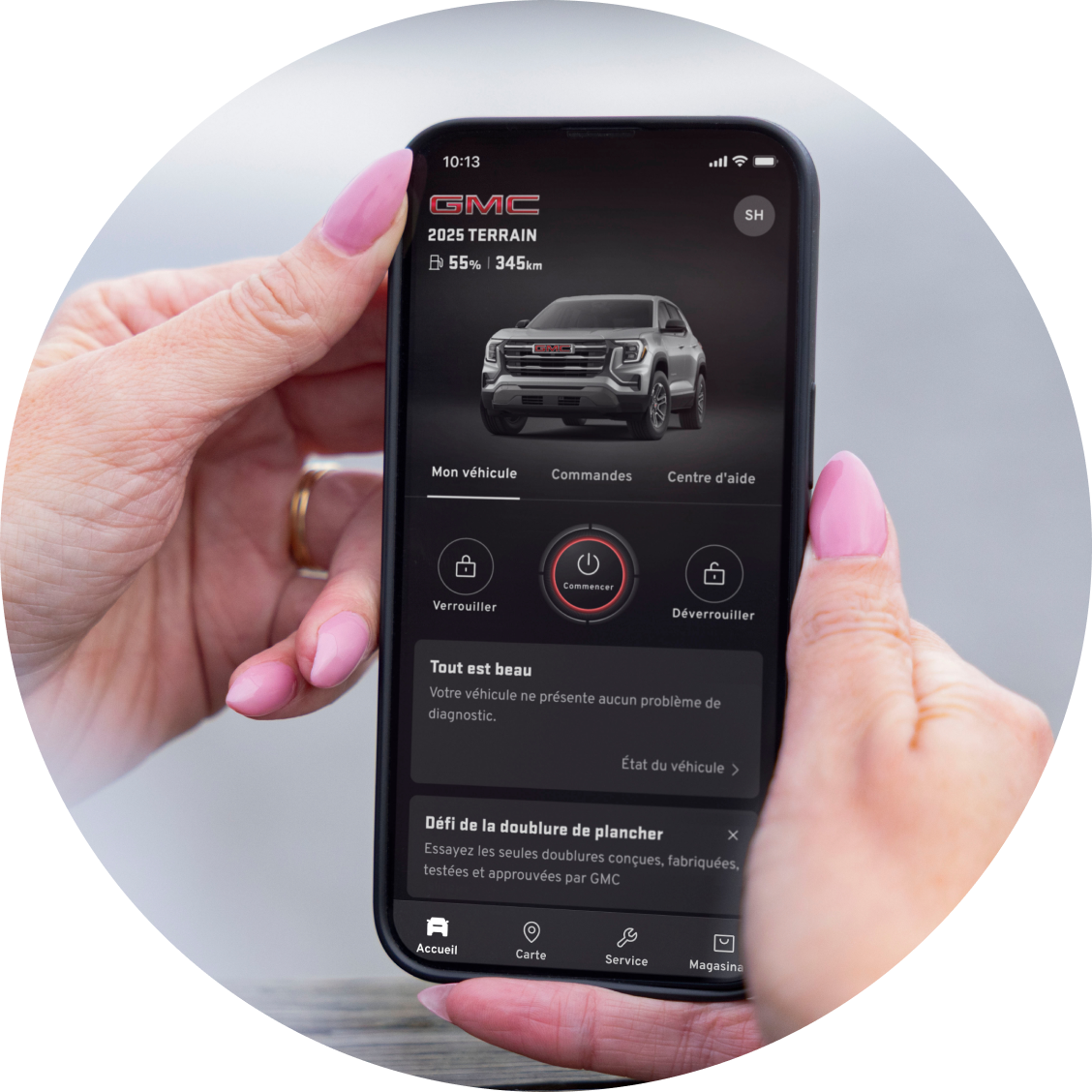 Des mains tiennent un smartphone affichant l'application GMC avec un modèle GMC Terrain 2025 et les commandes du véhicule.