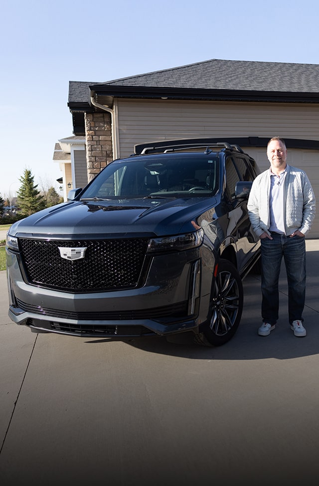 OnStar member Justin VanDyk smiling while standing next to his Cadillac Escalade SUV.